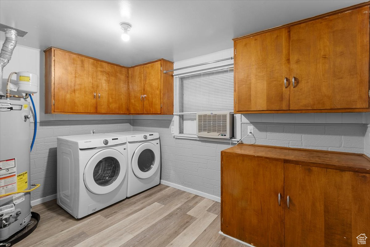 Clothes washing area featuring light wood-type flooring, independent washer and dryer, gas water heater, cabinets, and cooling unit