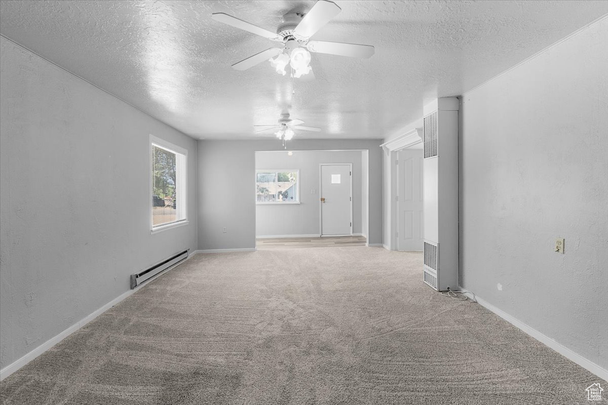 Carpeted spare room featuring baseboard heating, a textured ceiling, and ceiling fan