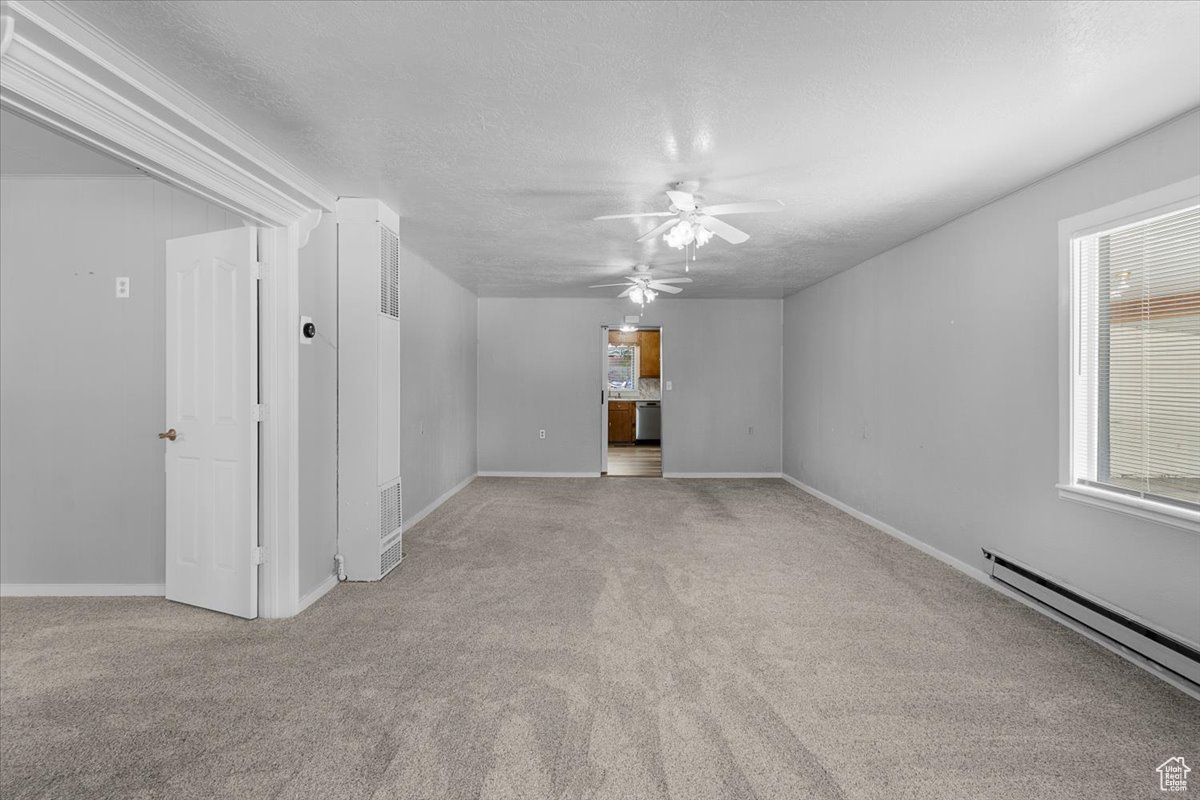 Unfurnished room featuring light colored carpet, a textured ceiling, ceiling fan, and a baseboard heating unit