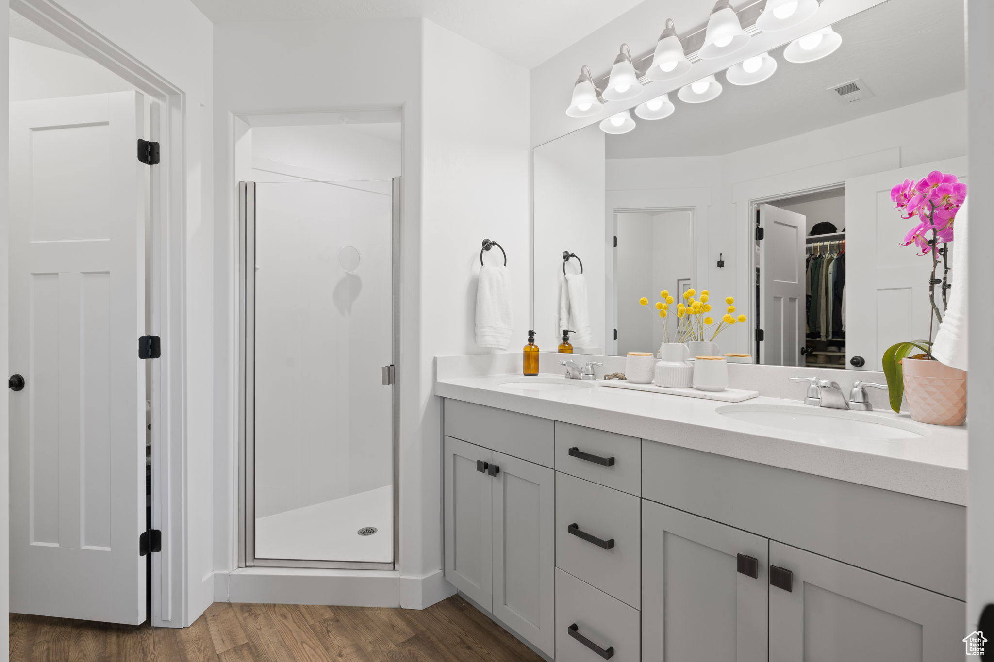 Bathroom with double vanity, a shower with door, and hardwood / wood-style floors