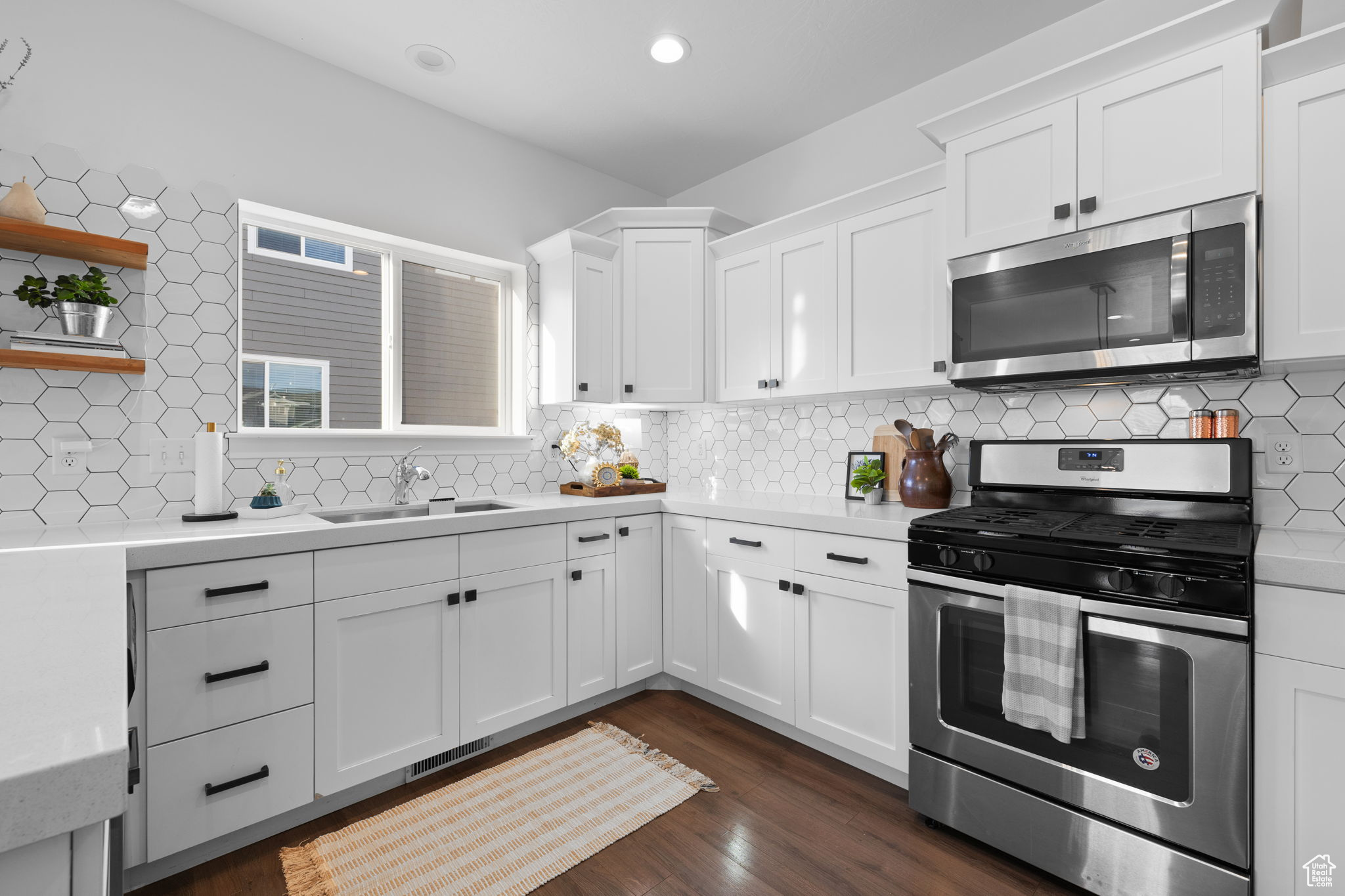 Kitchen with stainless steel appliances, dark wood-type flooring, backsplash, sink, and white cabinetry