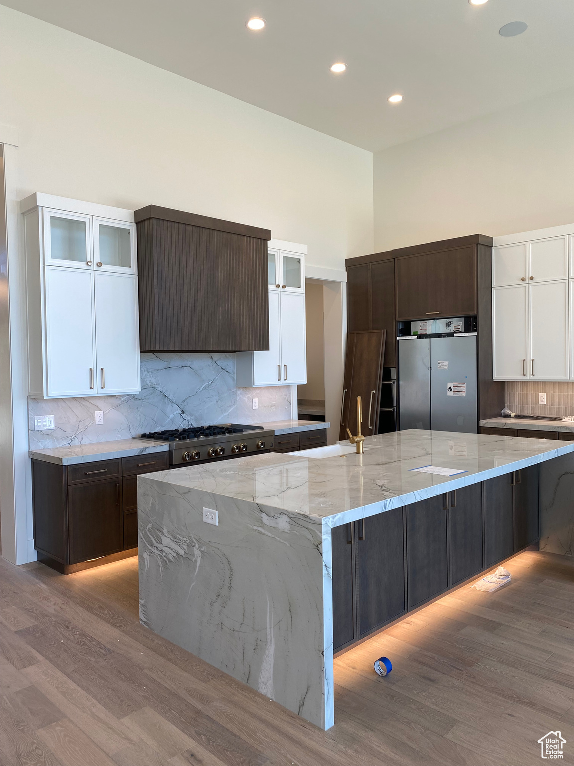 Kitchen featuring light wood-type flooring, stainless steel fridge, white cabinetry, and a spacious island