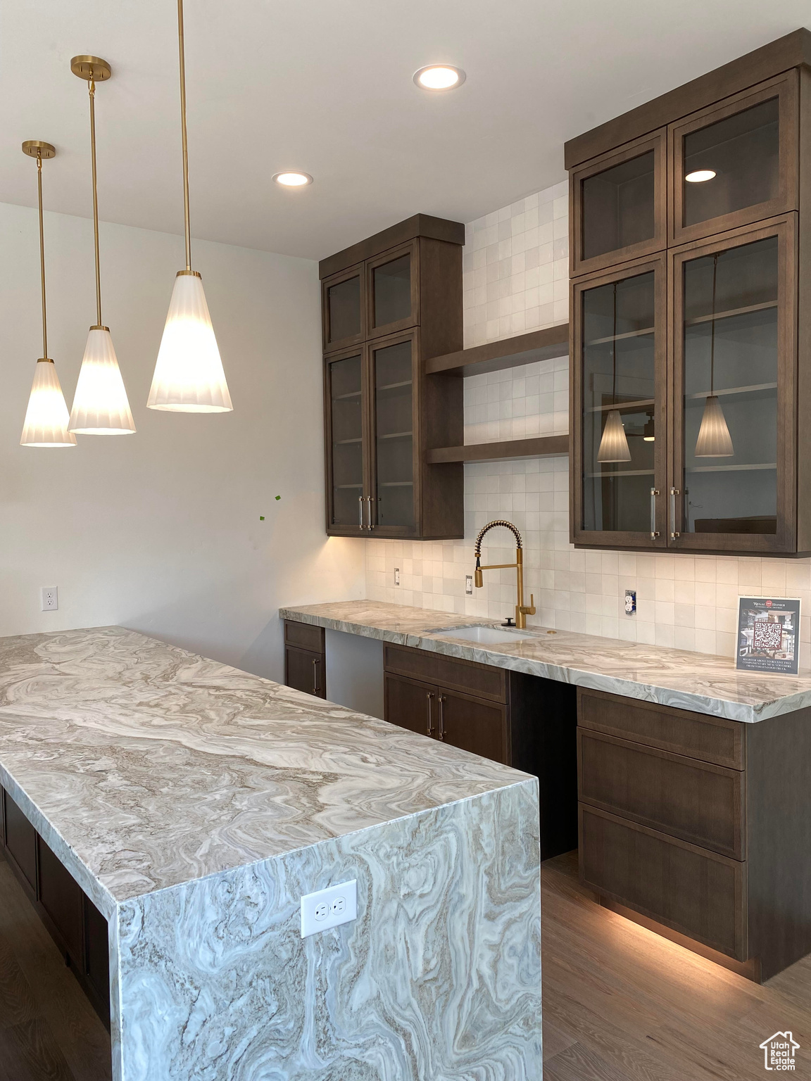 Kitchen featuring sink, light stone countertops, decorative backsplash, and hanging light fixtures