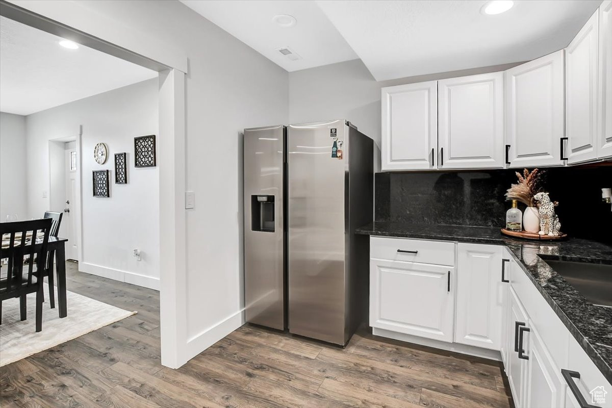 Kitchen with dark stone countertops, white cabinets, wood-type flooring, stainless steel refrigerator with ice dispenser, and tasteful backsplash