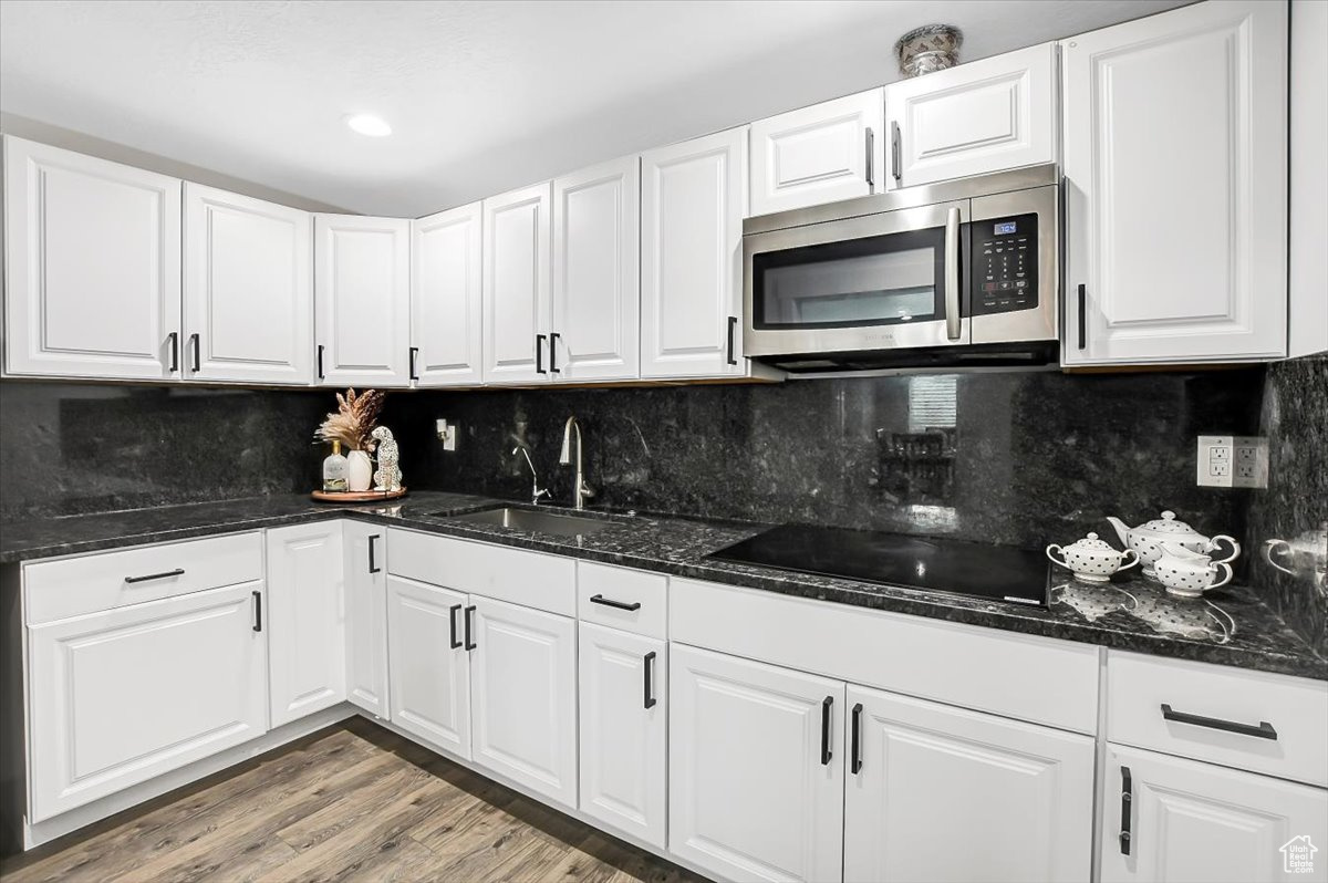 Kitchen with backsplash, white cabinets, sink, and light hardwood / wood-style flooring