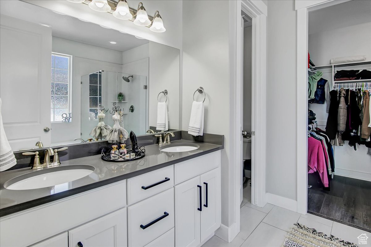 Bathroom featuring double vanity, tile flooring, walk in shower, and toilet