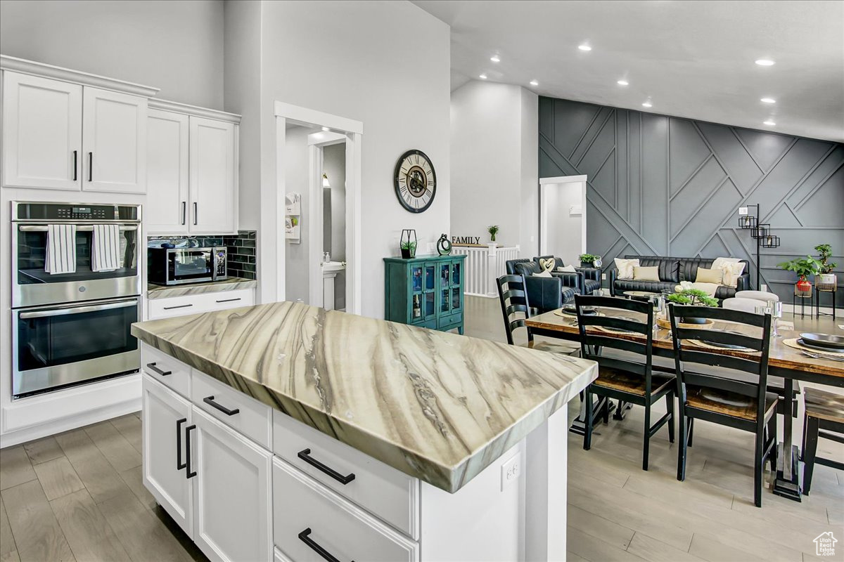 Kitchen featuring stainless steel double oven, white cabinets, backsplash, and light hardwood / wood-style floors