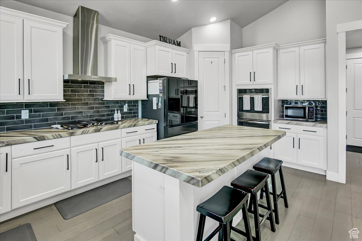 Kitchen featuring a center island, wall chimney range hood, lofted ceiling, stainless steel appliances, and tasteful backsplash