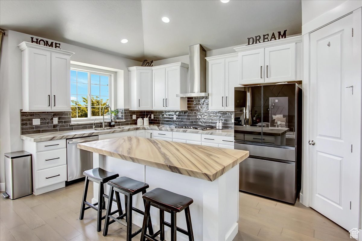 Kitchen featuring a center island, wall chimney exhaust hood, tasteful backsplash, and appliances with stainless steel finishes