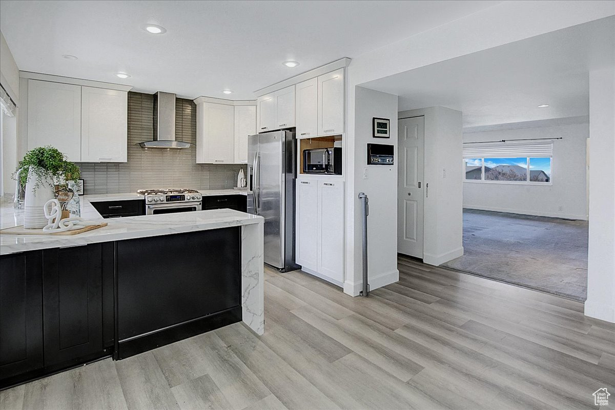 Kitchen featuring appliances with stainless steel finishes, wall chimney range hood, tasteful backsplash, and light wood-type flooring