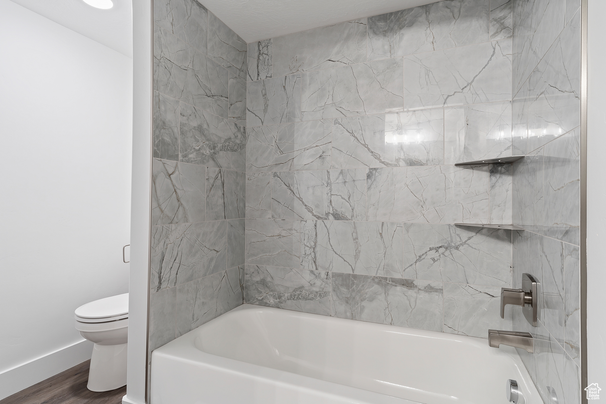 Bathroom with tiled shower / bath, wood-type flooring, and toilet