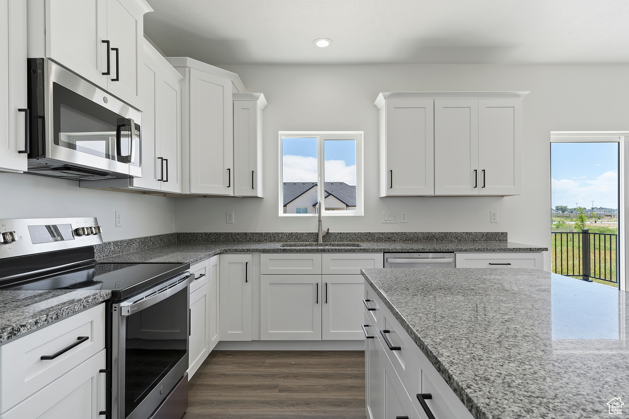 Kitchen with dark hardwood / wood-style flooring, appliances with stainless steel finishes, sink, and white cabinets