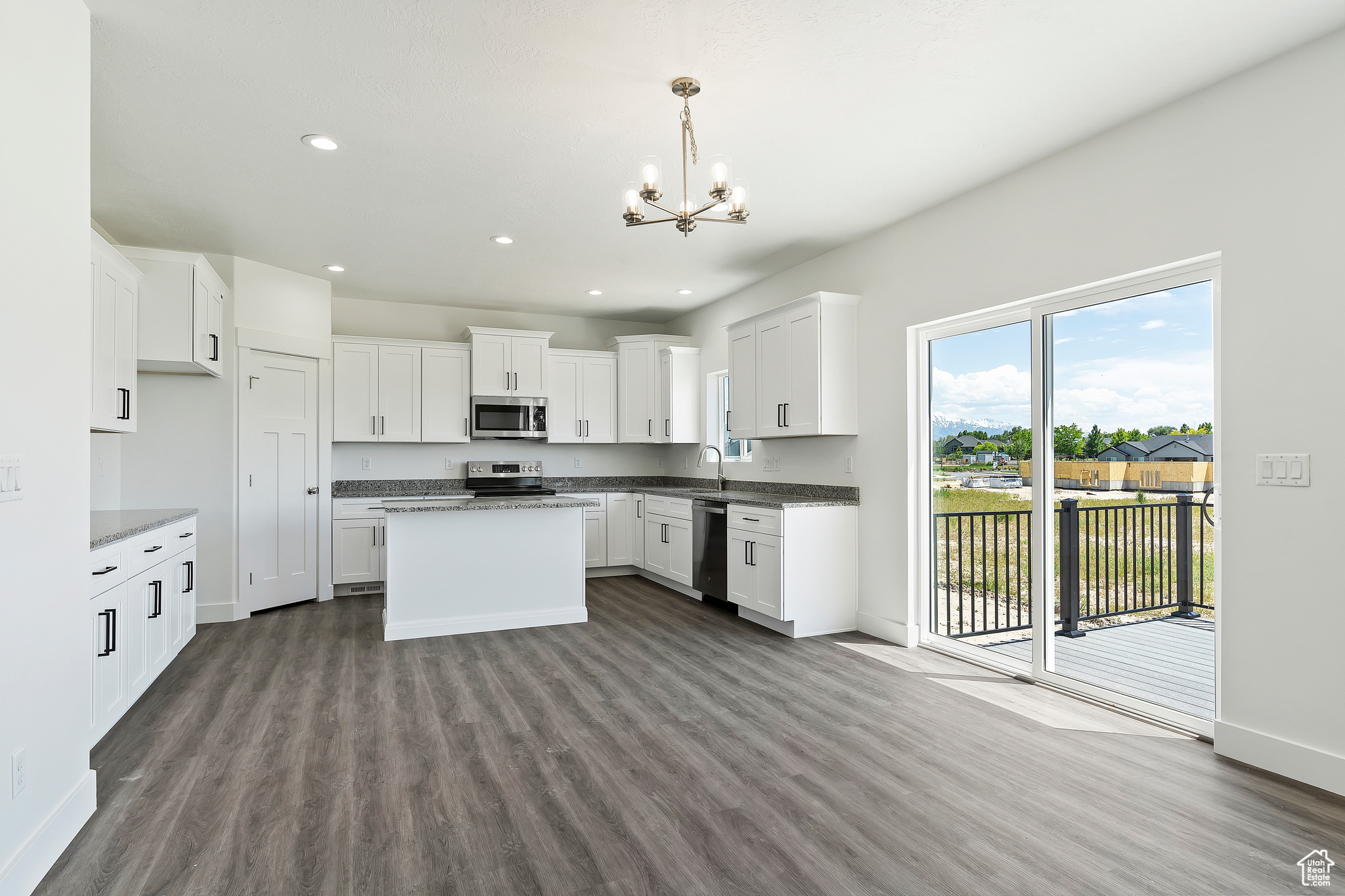 Kitchen featuring appliances with stainless steel finishes, white cabinets, pendant lighting, and hardwood / wood-style floors