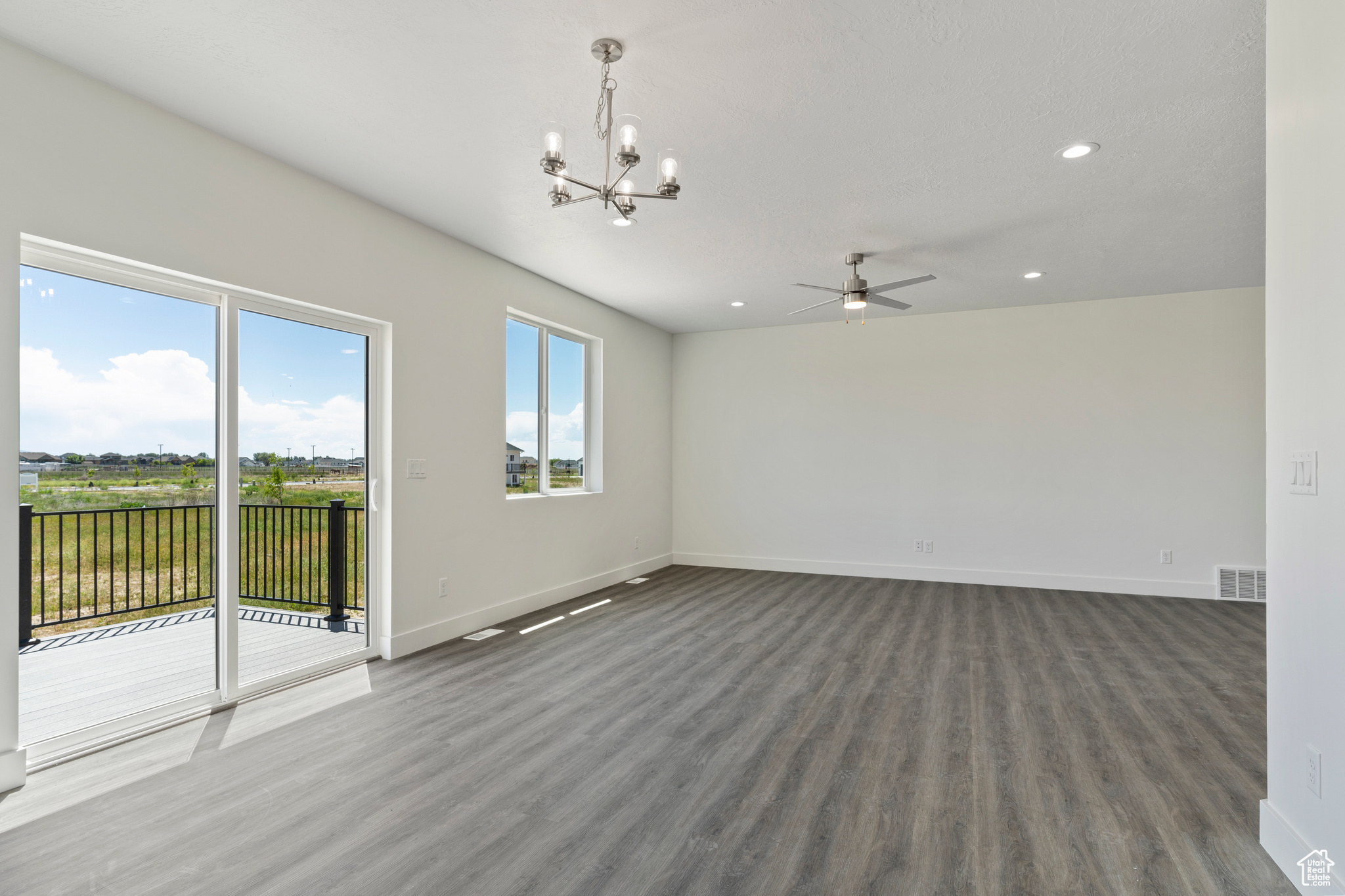 Spare room featuring hardwood / wood-style flooring and ceiling fan with notable chandelier