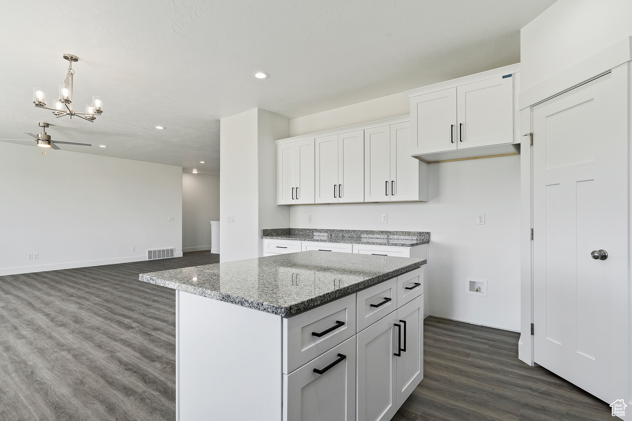 Kitchen featuring decorative light fixtures, dark wood-type flooring, ceiling fan with notable chandelier, a kitchen island, and white cabinetry