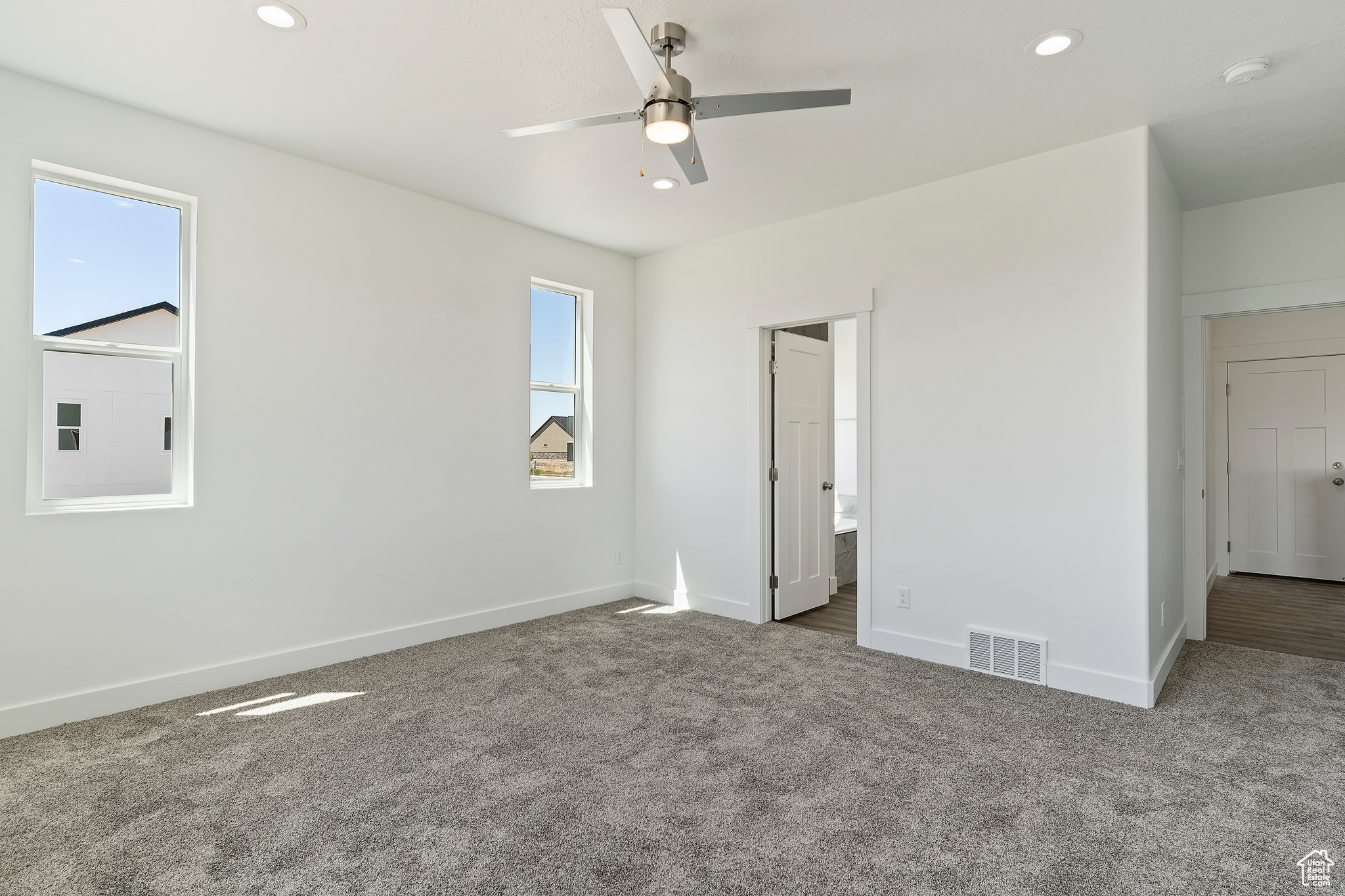 Unfurnished bedroom with carpet, multiple windows, ensuite bath, and ceiling fan