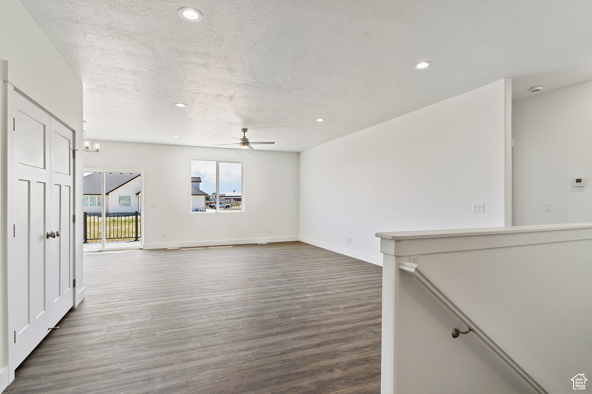 Unfurnished living room featuring dark wood-type flooring, a textured ceiling, and ceiling fan with notable chandelier