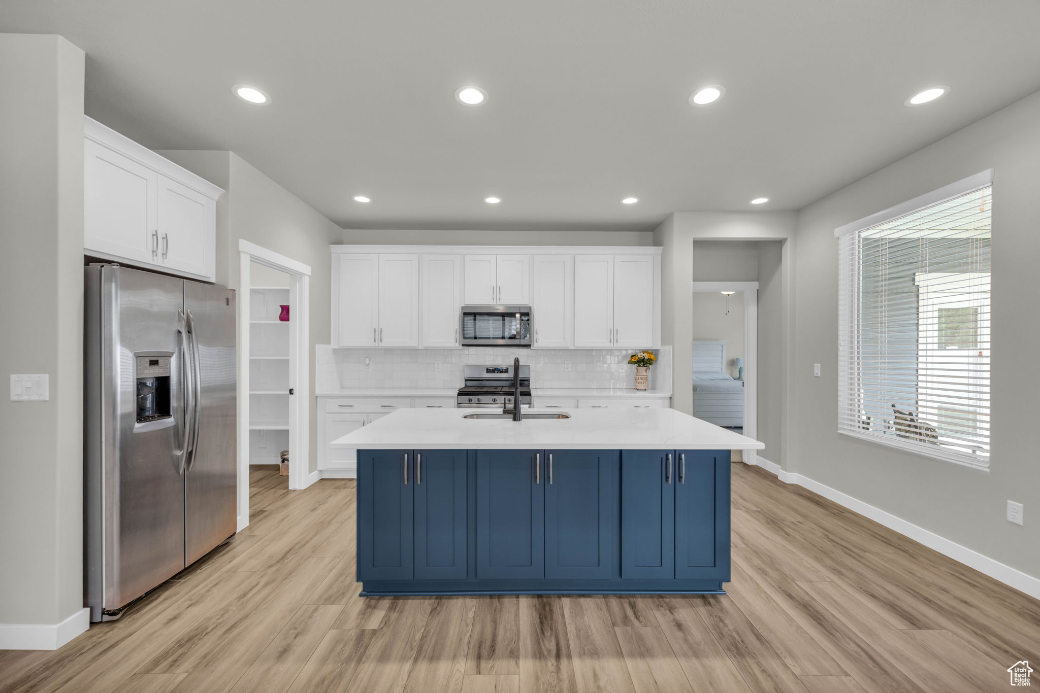 Kitchen featuring light hardwood / wood-style floors, appliances with stainless steel finishes, an island with sink, white cabinets, and backsplash