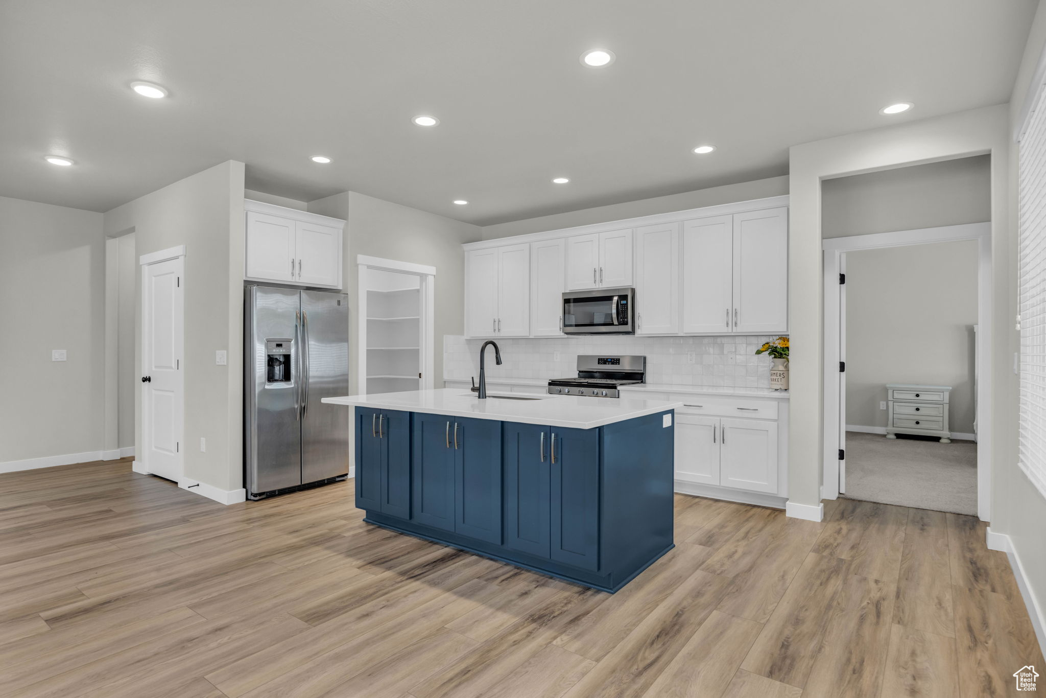 Kitchen with appliances with stainless steel finishes, a kitchen island with sink, light hardwood / wood-style floors, and tasteful backsplash