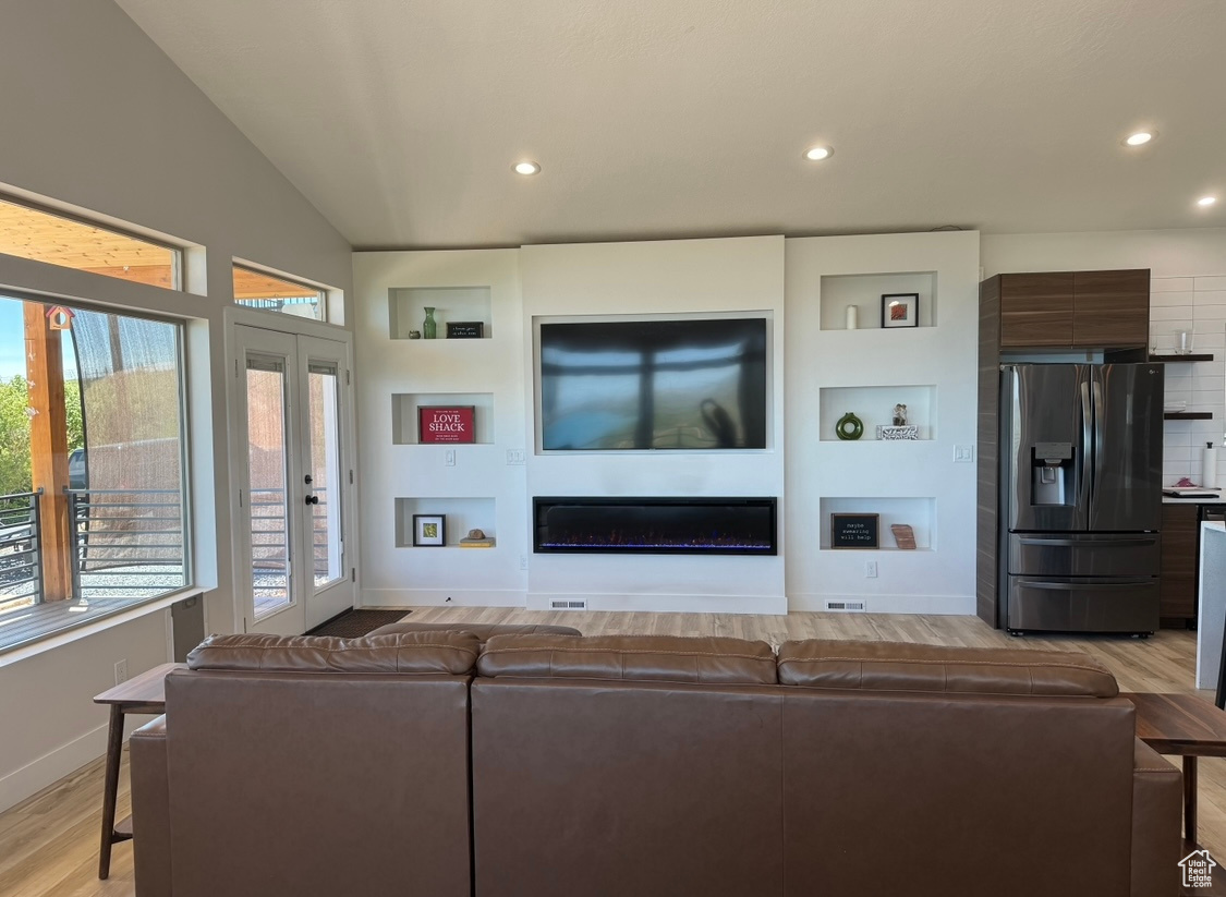 Living room with vaulted ceiling, built in shelves, and light wood-type flooring