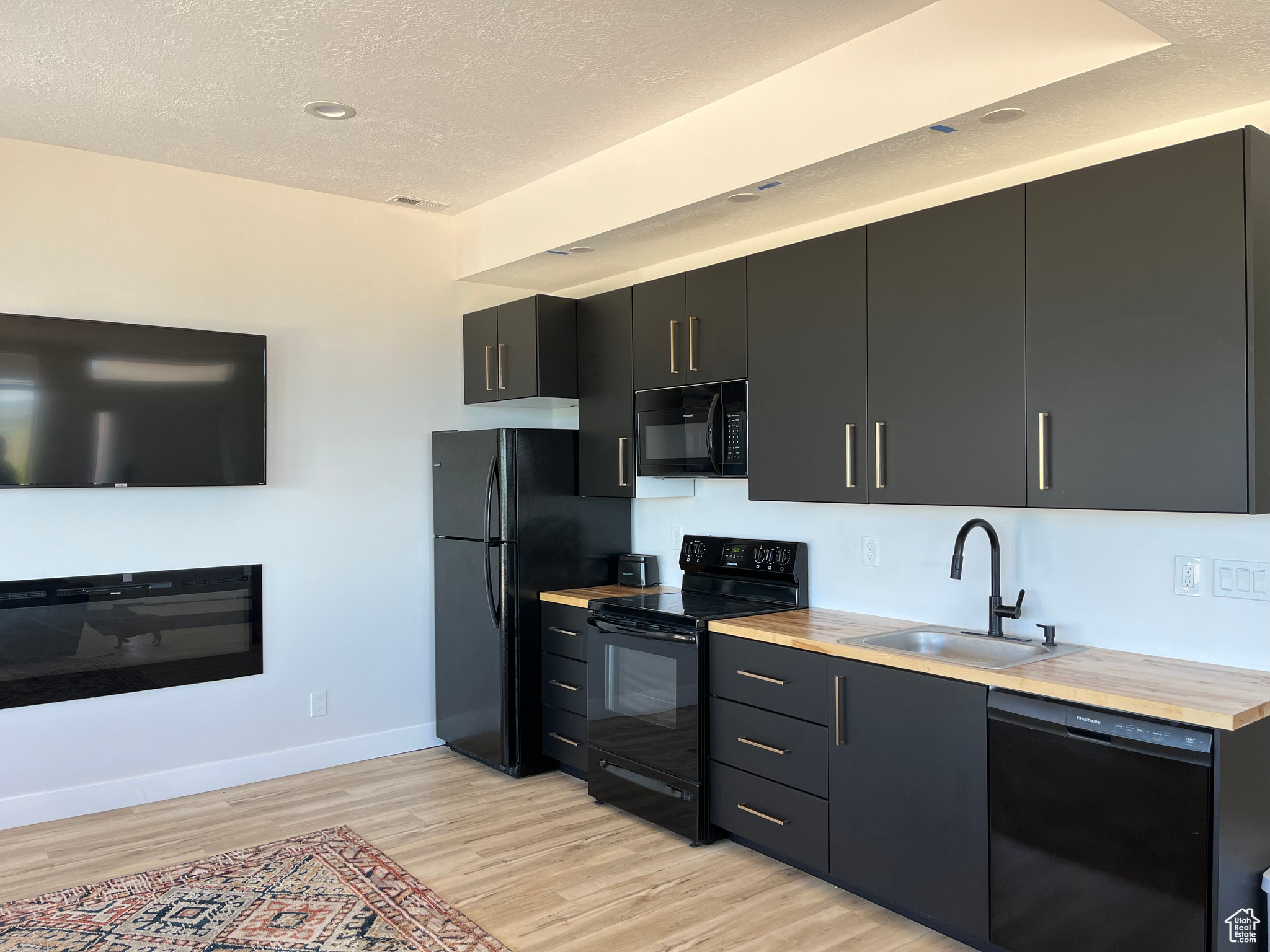 Lower level Kitchen with light hardwood / wood-style floors, black appliances, wooden counters, sink, and a textured ceiling