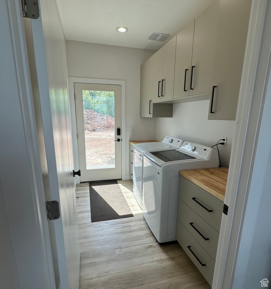 Washroom with washing machine and dryer, light hardwood / wood-style flooring, and cabinets