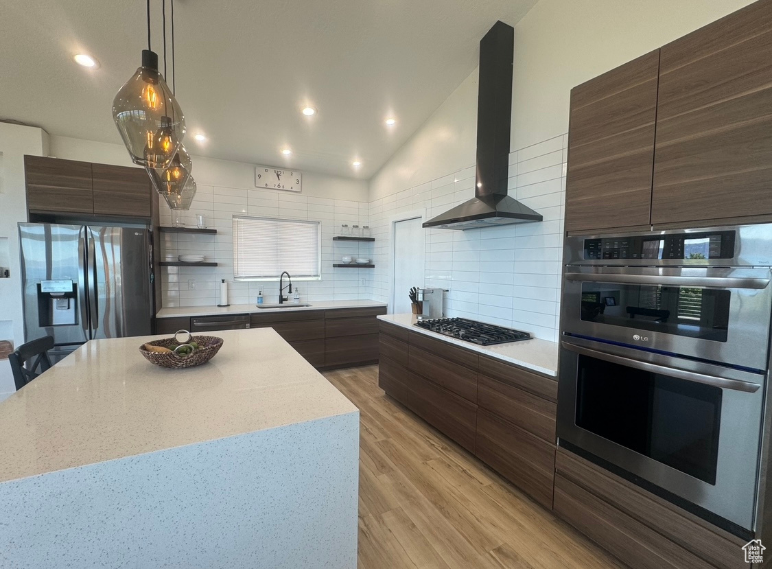 Kitchen featuring light hardwood / wood-style floors, a kitchen island, backsplash, wall chimney range hood, and appliances with stainless steel finishes