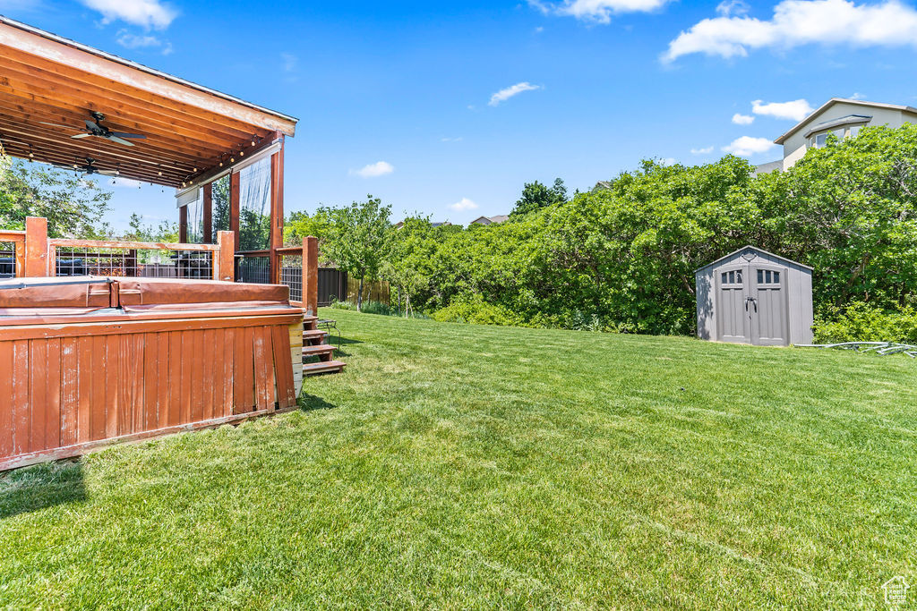 View of yard with ceiling fan, a shed, and a hot tub