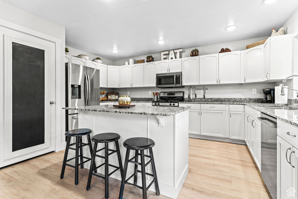 Kitchen featuring waterproof vinyl floor, Granite Countertops, Single Basin Sink with Sprayer, a kitchen island, a breakfast bar, and stainless steel appliances