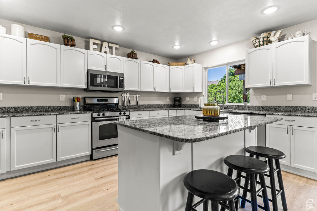 Kitchen featuring waterproof vinyl floor, Granite Countertops, Single Basin Sink with Sprayer, a kitchen island, a breakfast bar, and stainless steel appliances