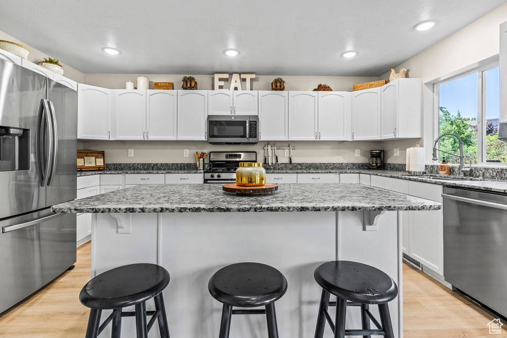 Kitchen featuring waterproof vinyl floor, Granite Countertops, Single Basin Sink with Sprayer, a kitchen island, a breakfast bar, and stainless steel appliances