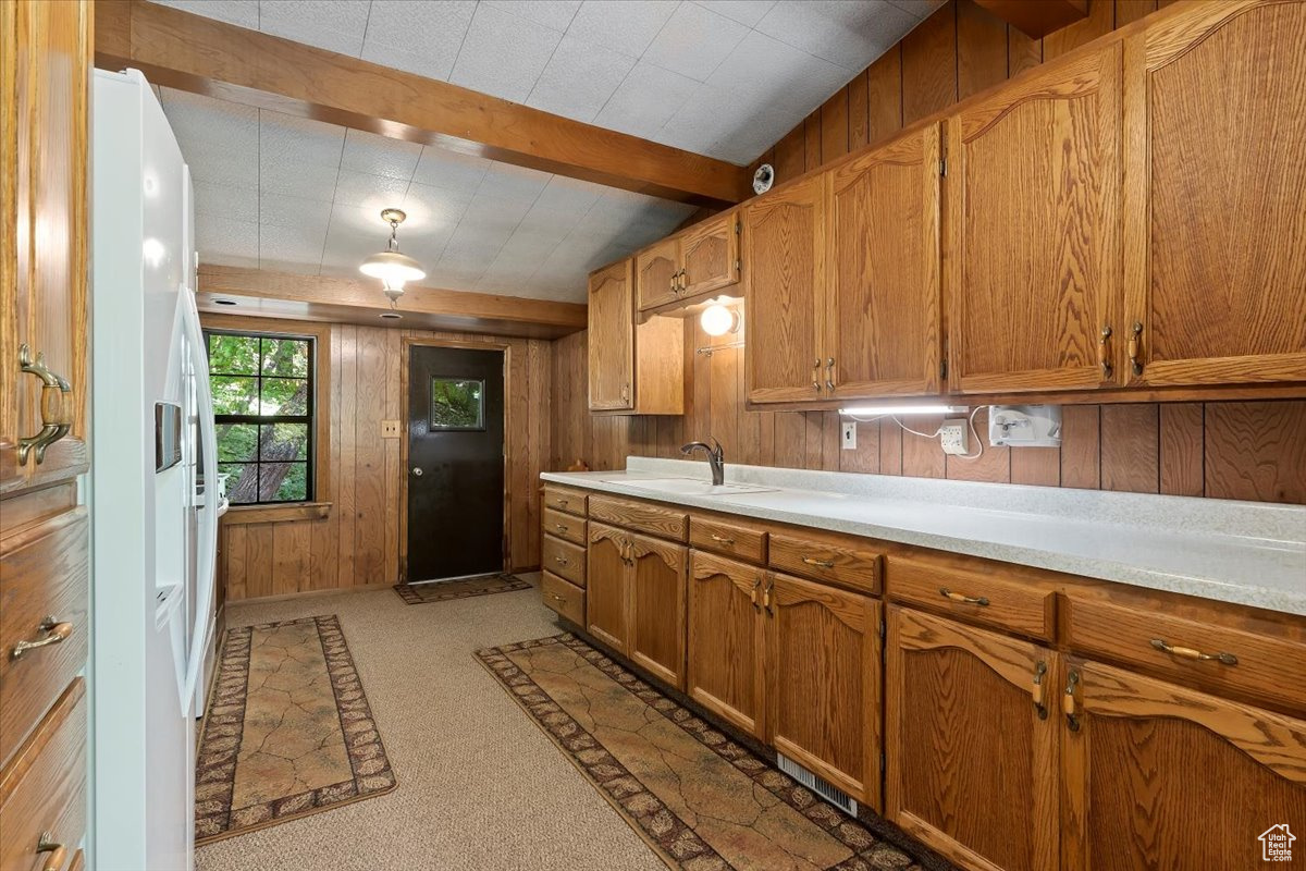 Kitchen featuring light warm on the feet carpet, wood walls, sink, and beamed ceiling.