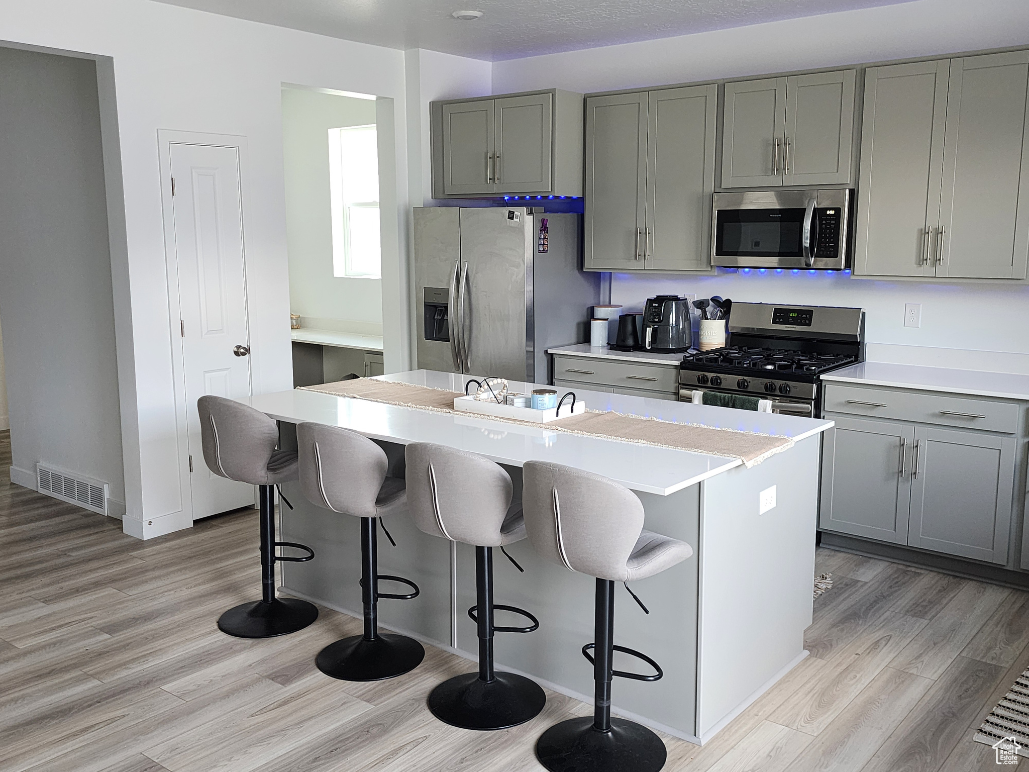 Kitchen featuring light hardwood / wood-style flooring, gray cabinets, a center island, a breakfast bar, and appliances with stainless steel finishes