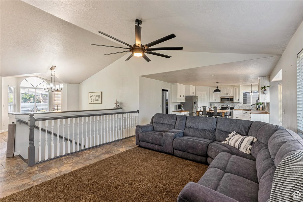 Tiled living room featuring vaulted ceiling, sink, and ceiling fan with notable chandelier