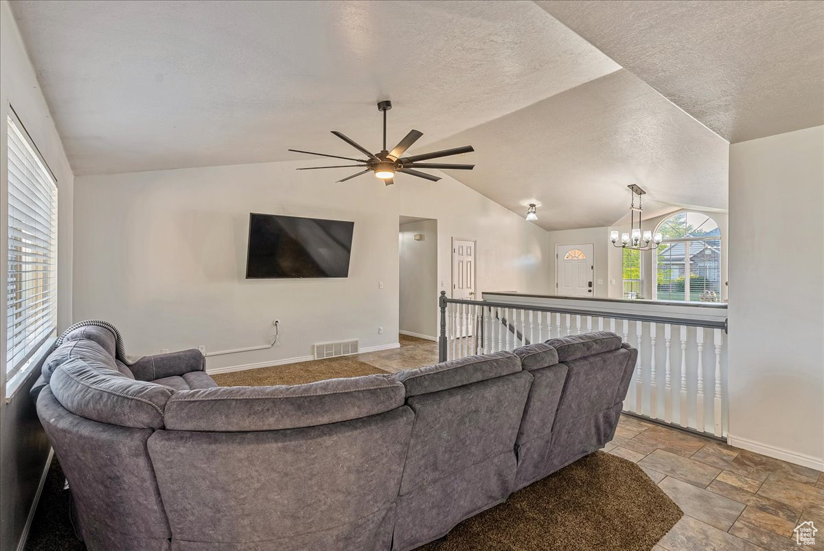 Living room featuring tile floors, ceiling fan with notable chandelier, a textured ceiling, and lofted ceiling