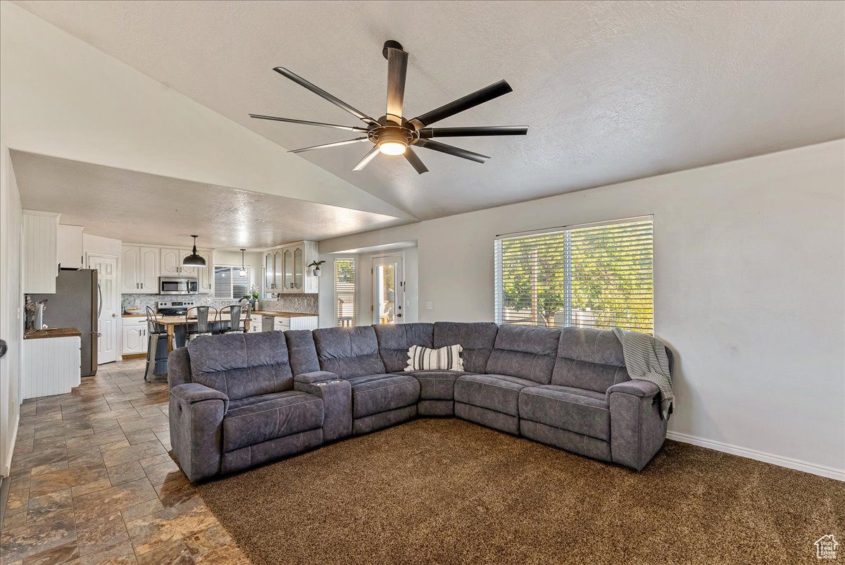 Living room featuring ceiling fan, lofted ceiling, and dark tile floors