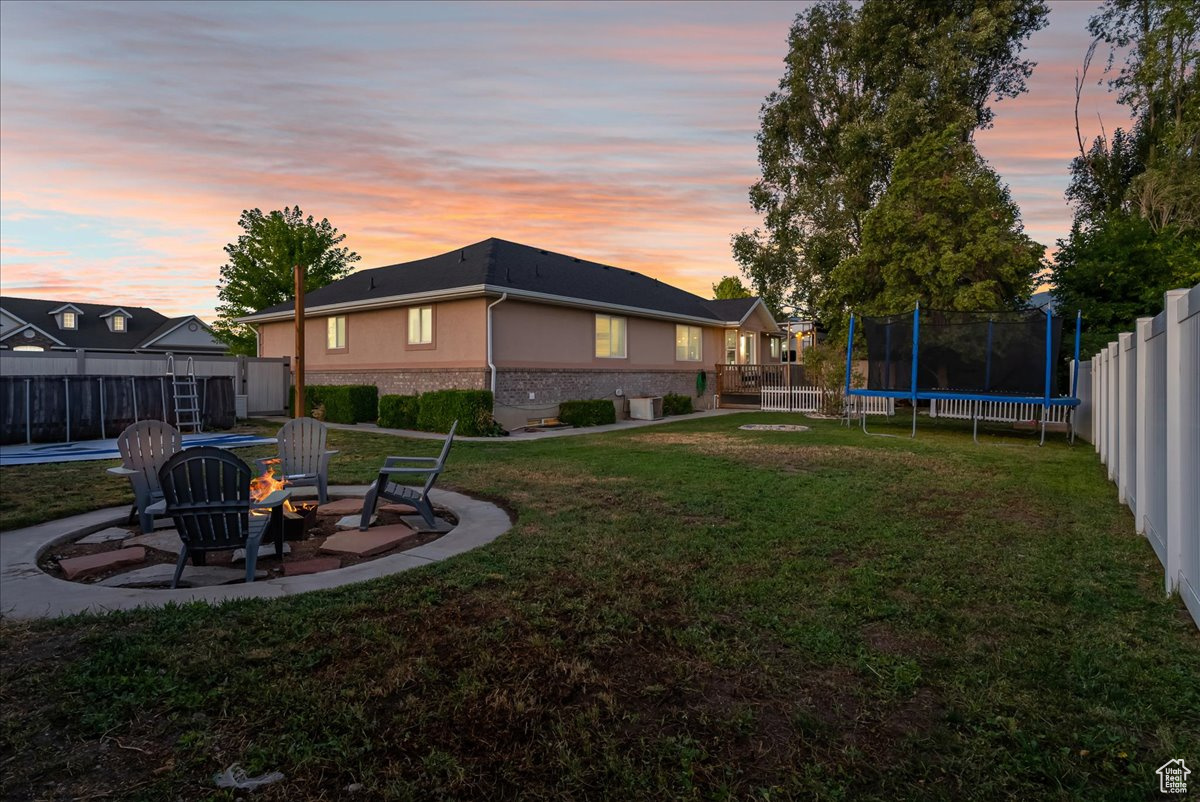 Yard at dusk featuring a trampoline, a patio area, and an outdoor fire pit