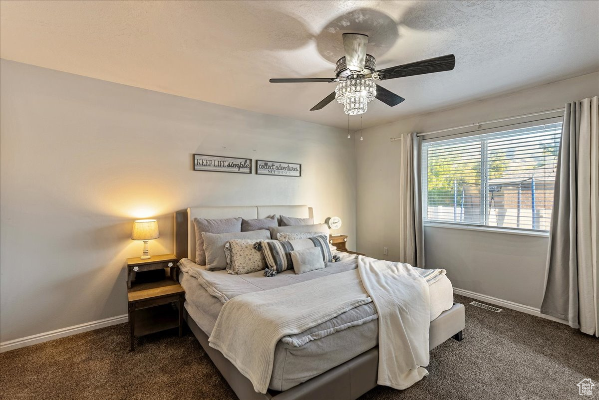 Bedroom featuring dark colored carpet, ceiling fan, and a textured ceiling