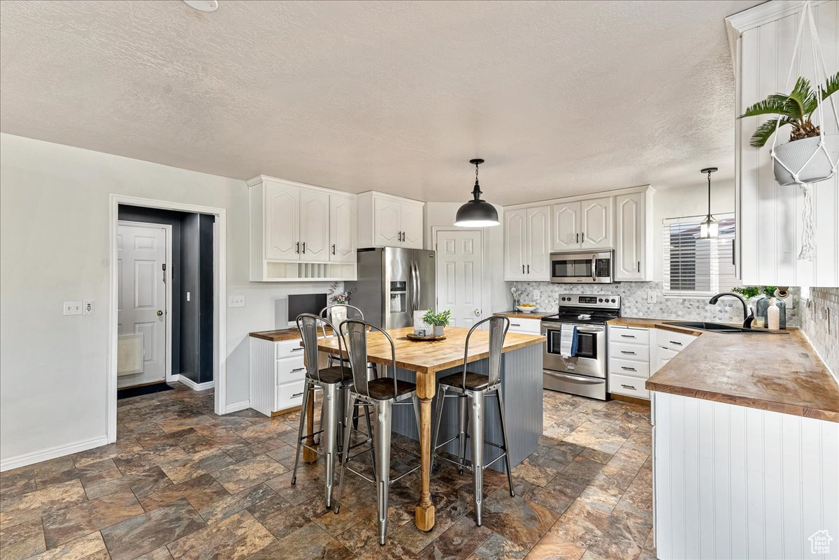 Kitchen with stainless steel appliances, white cabinets, sink, and wooden counters