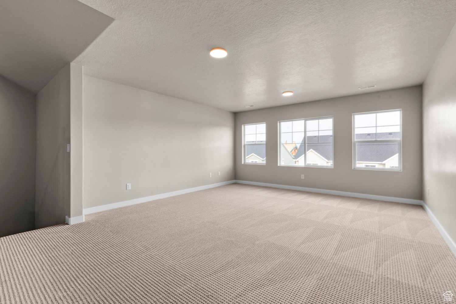 Empty room with a textured ceiling and light colored carpet