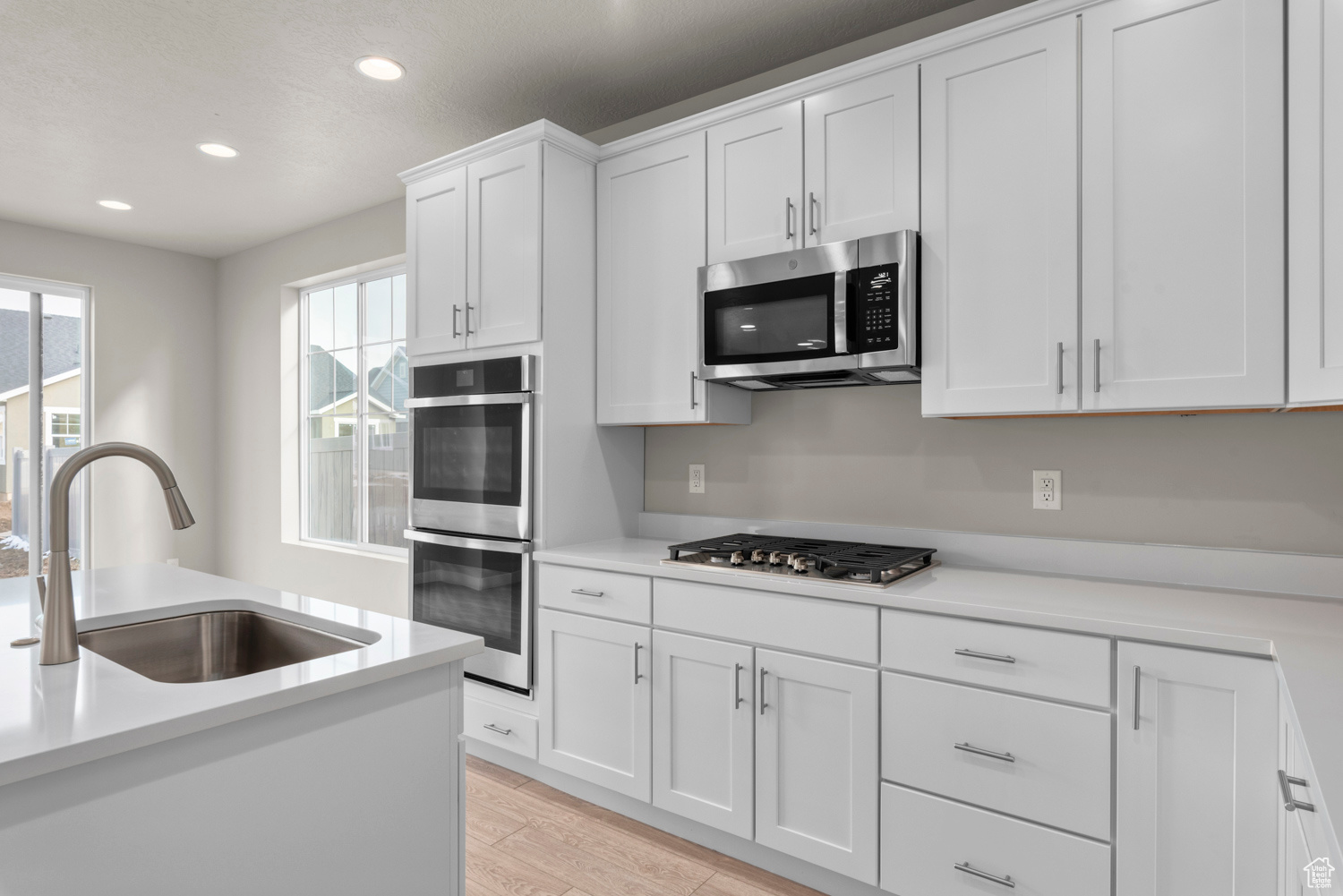 Kitchen with sink, light hardwood / wood-style floors, white cabinets, and appliances with stainless steel finishes