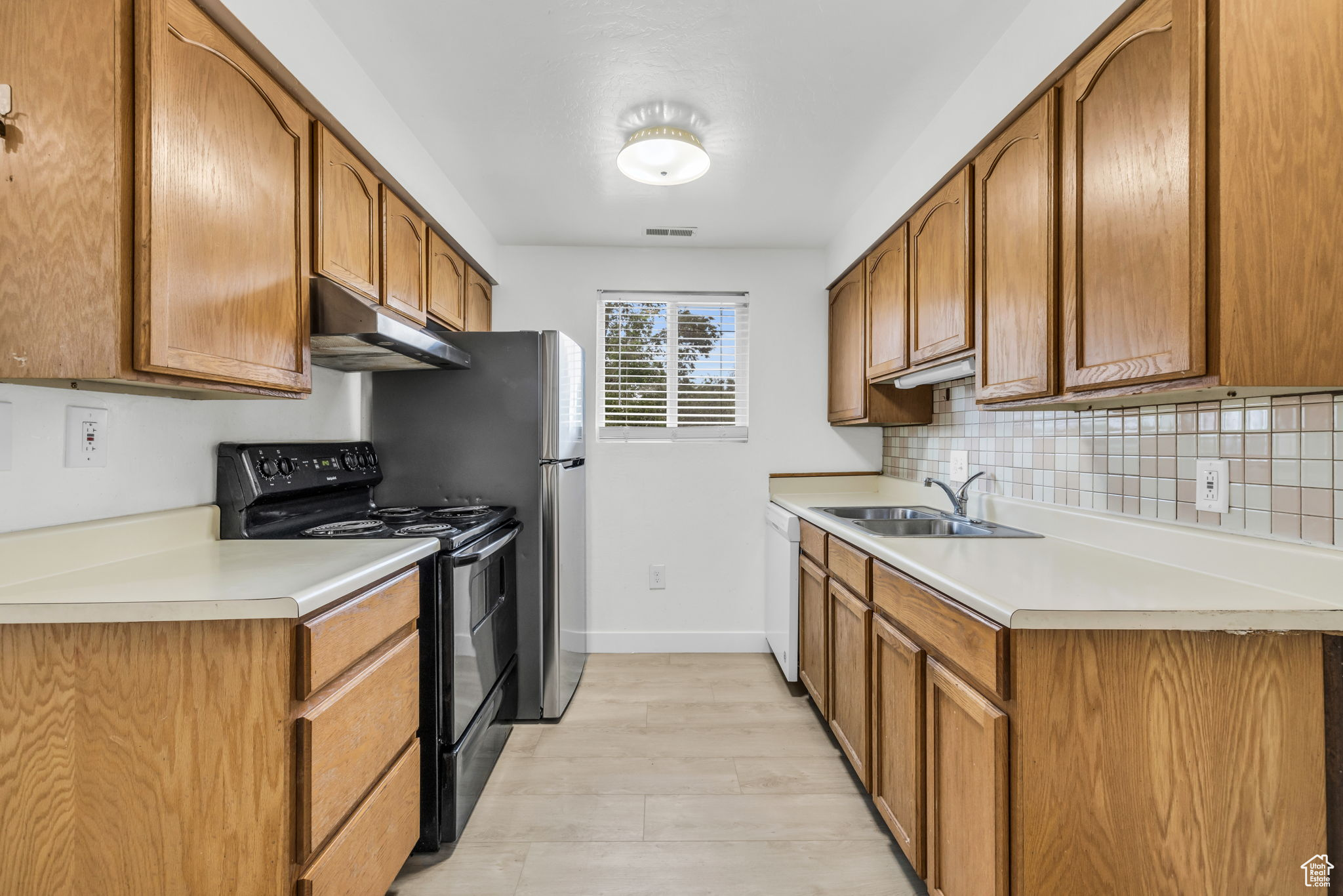 Kitchen with light hardwood / wood-style floors, black range with electric stovetop, stainless steel refrigerator, backsplash, and sink