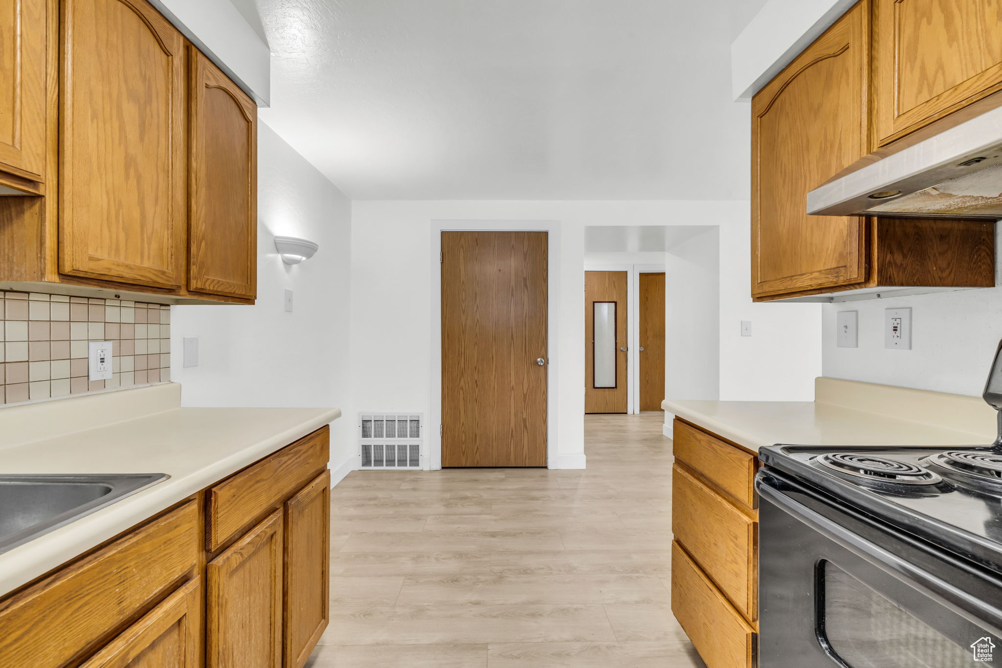 Kitchen featuring black range with electric stovetop, light hardwood / wood-style flooring, and tasteful backsplash