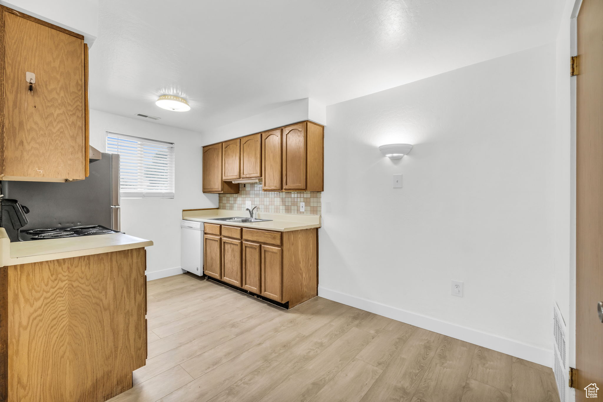 Kitchen with dishwasher, sink, light hardwood / wood-style floors, and tasteful backsplash