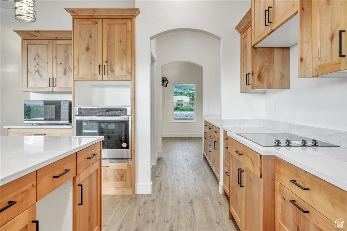 Kitchen with black electric stovetop, oven, light brown cabinetry, and light hardwood / wood-style flooring