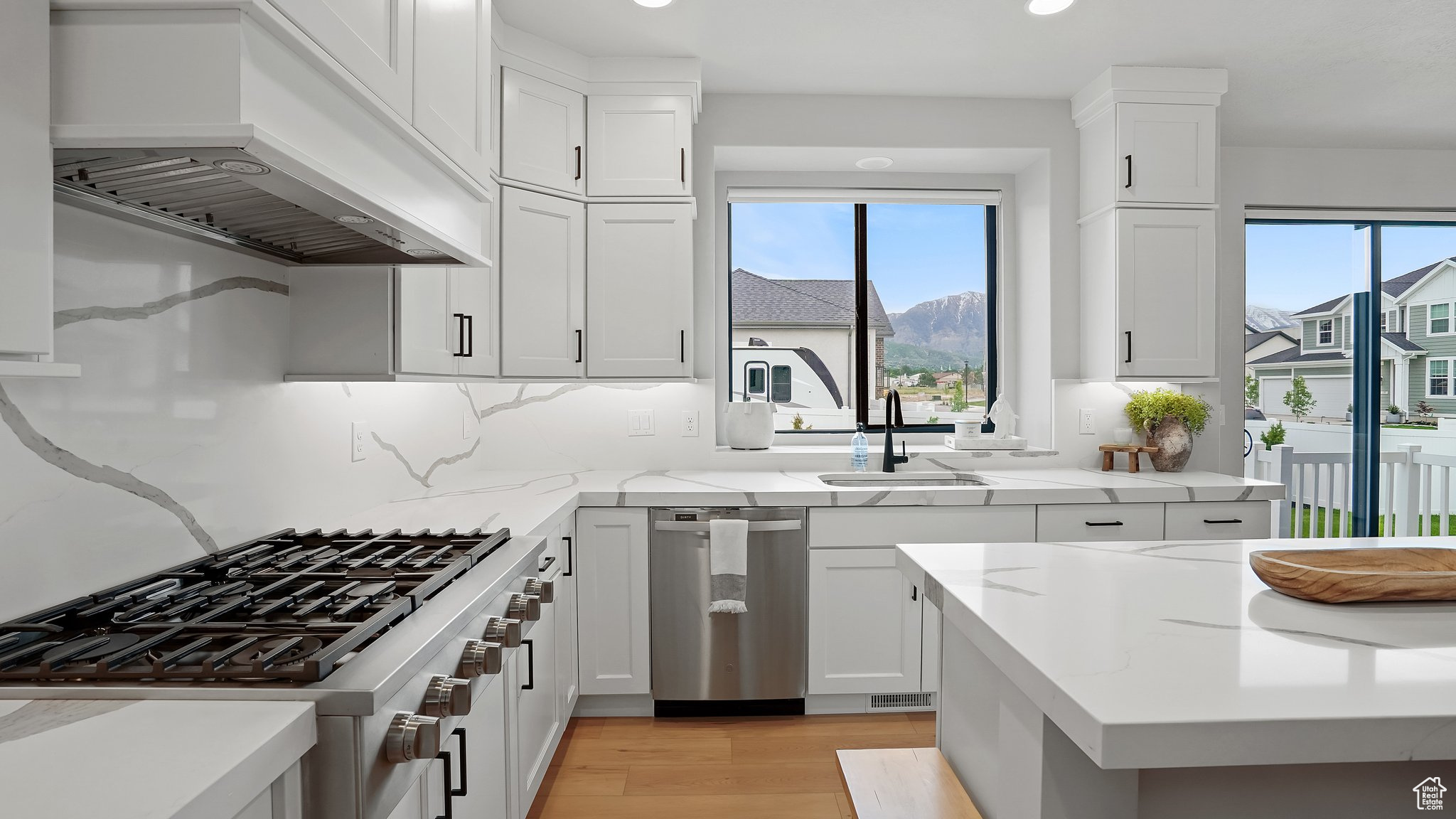 Kitchen featuring custom range hood, light hardwood / wood-style flooring, backsplash, range, and sink