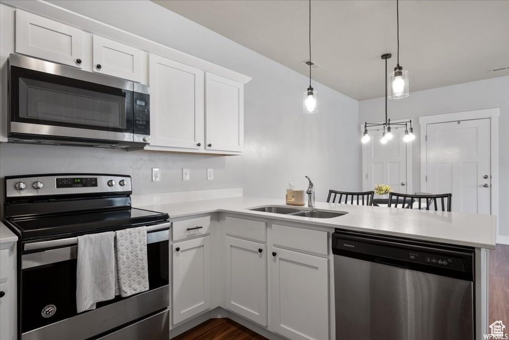 Kitchen featuring decorative light fixtures, white cabinetry, sink, dark hardwood / wood-style floors, and appliances with stainless steel finishes