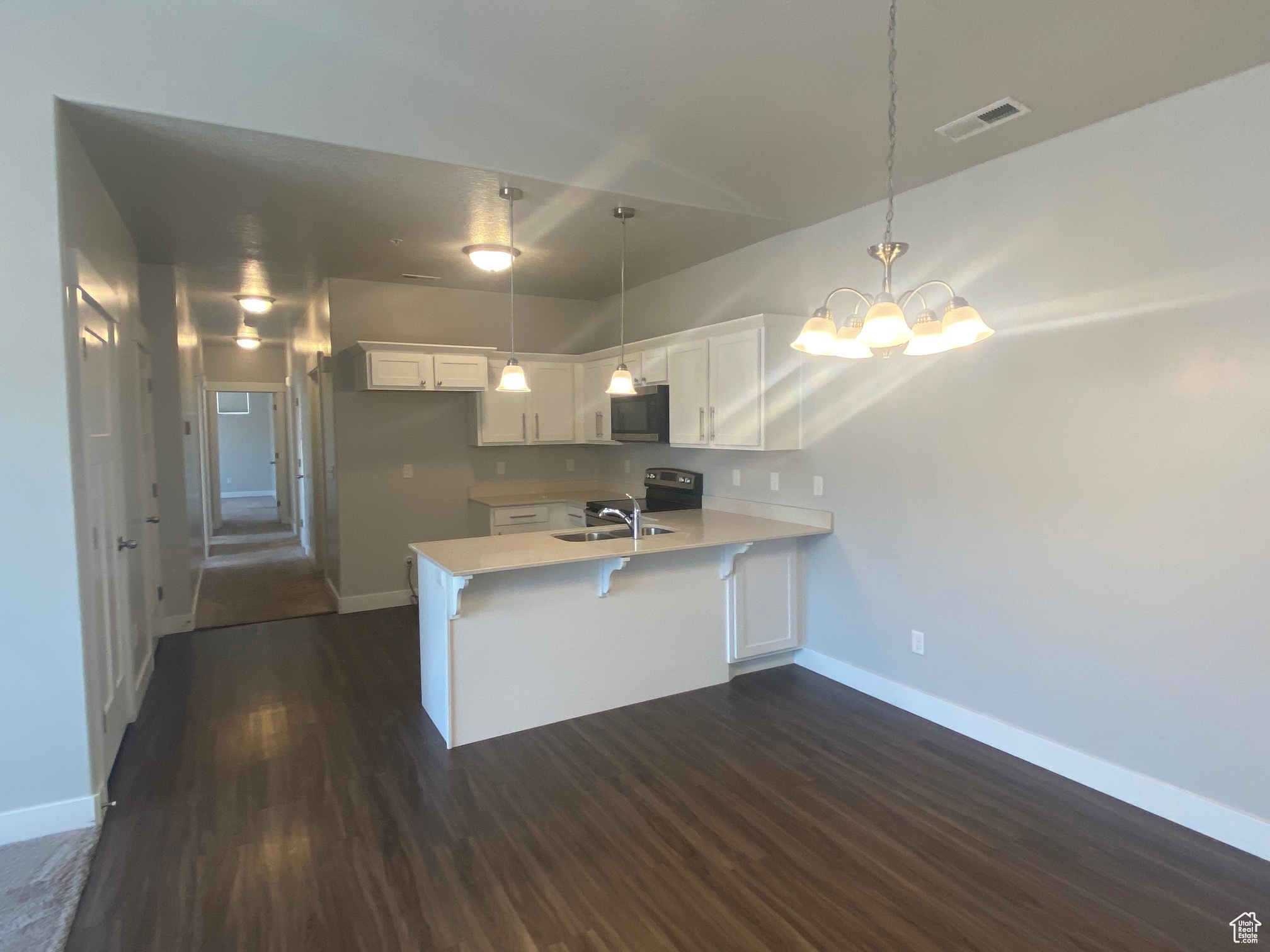 Kitchen with pendant lighting, dark wood-type flooring, kitchen peninsula, sink, and white cabinets