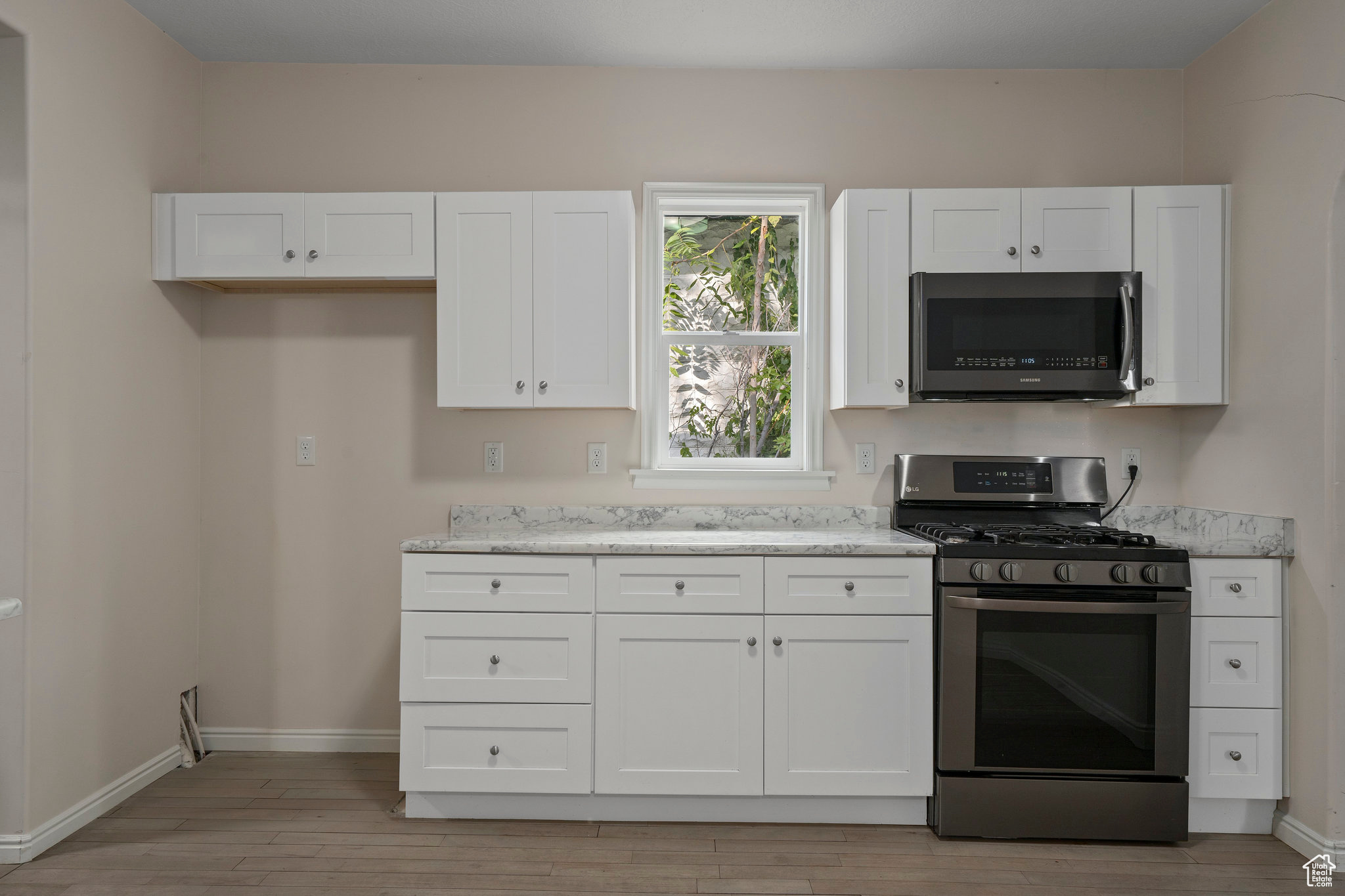 Kitchen featuring light stone countertops, stainless steel appliances, light hardwood / wood-style floors, and white cabinetry