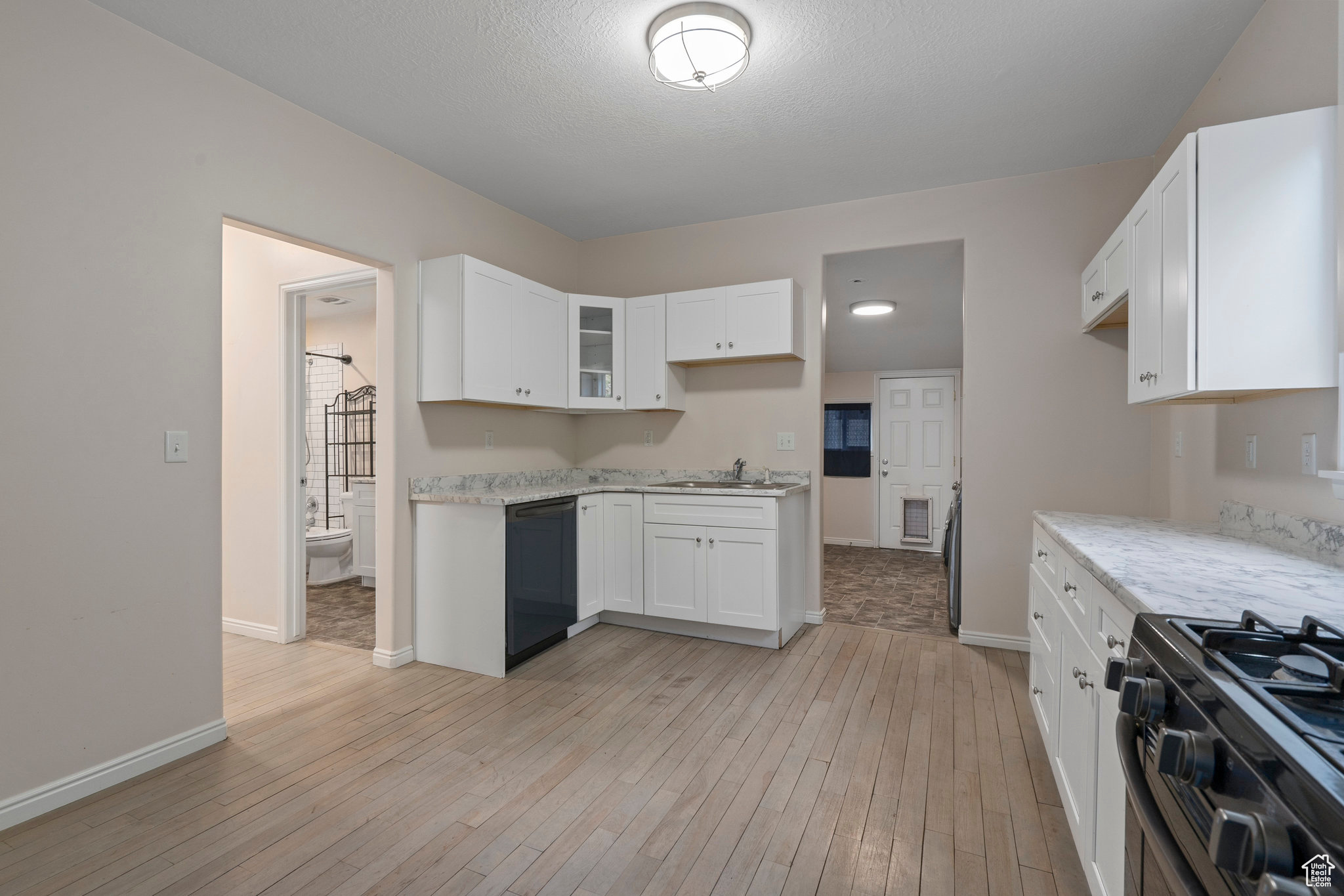 Kitchen featuring sink, light hardwood / wood-style floors, black dishwasher, white cabinets, and stainless steel gas range